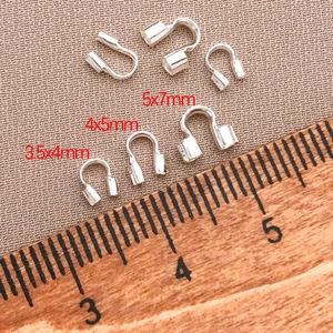Three sizes of silver U-shape wire protectors for jewelry making next to a wooden ruler