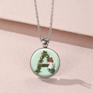 Close-up of glass pendant necklace featuring green letter A and small snowman illustration