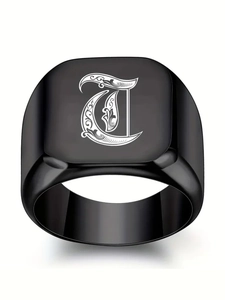 Gros plan sur bague chevalière noire avec lettre gothique T et motifs floraux gravés