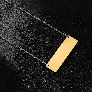 Polished gold rectangular bar pendant necklace on a dark textured stone background