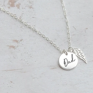 Close-up of stainless steel DAD pendant necklace with angel wing charm on wood