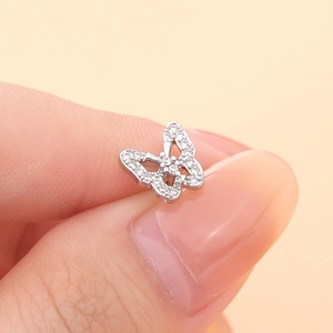 Macro shot of silver butterfly ear stud with micro-set white zircon on pink background