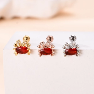 Detailed close-up of crab-shaped earrings in gold, silver and rose gold with red zircon