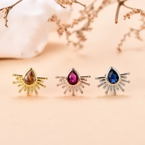 Primer plano de pendientes de gota con gemas en acabados dorado, oro rosa y plata