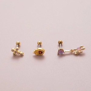 Detail of gold piercing studs featuring crystal cross, red heart and purple gem designs
