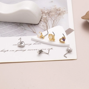 Detailaufnahme von L-förmigen Titan-Nasensteckern mit buntem Zirkonherz und Opal-Designs