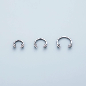 Three sizes of 316L stainless steel horseshoe rings with spiked ends on blue background