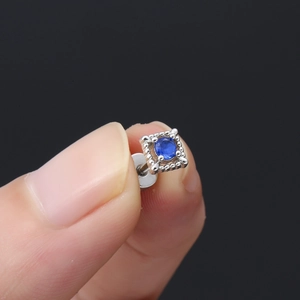 Macro-opname van zilveren vierkante oorsteker met blauwe zirkoon en milgrain-details