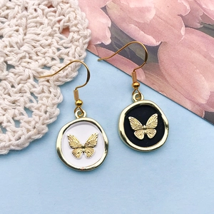 Detail view of round enamel butterfly charms with gold trim in black and white finish