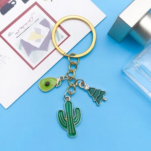 Détail d'un porte-clés doré avec breloques émaillées de cactus, avocat et sapin vert