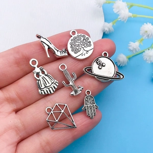 Detail of vintage silver alloy charms for DIY jewelry held in hand to show the actual scale