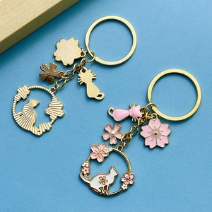 Close-up of enamel pink cherry blossom and pearl cat keychains with gold-plated finish