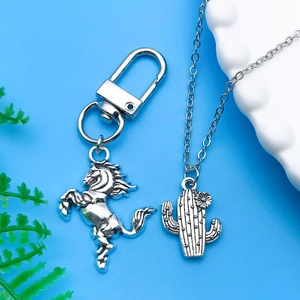 Detail of silver cowboy horse keychain and cactus pendant necklace on blue background