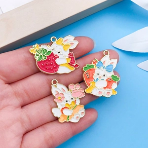 Detail of three cute enamel Easter bunny charms with carrots and flowers held by a hand