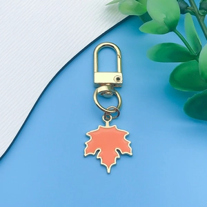 Detailed close-up of orange enamel maple leaf pendant with gold lobster clasp and key ring