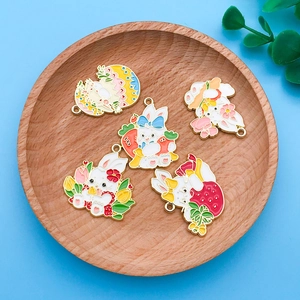 Nahaufnahme bunter Osterhasen-Emaille-Anhänger mit Blumen- und Fruchtmotiven auf Holztablett