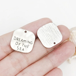 Close-up of silver sea charms with Dreaming of the Sea engraving for DIY jewelry