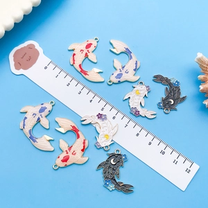 Macro detail of enamel koi fish pendants with dimensions shown on a ruler