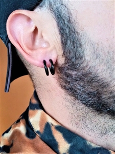 Détail de boucles d'oreilles créoles noires en acier portées par un homme