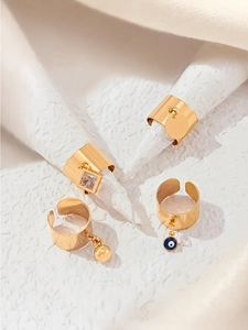 Détail de quatre bagues ouvertes dorées avec zircon, œil bleu et pendentifs ronds