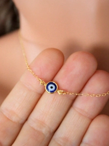 Gros plan d'un collier doré délicat avec un pendentif œil bleu porté aux doigts
