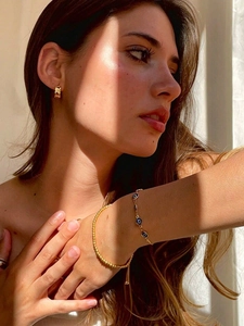 Détail de bracelets en perles dorées avec charme œil maléfique et boucles d'oreilles créoles