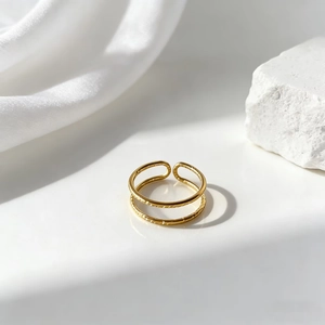Detalle de anillo de doble capa en acero inoxidable dorado con textura sobre fondo de piedra