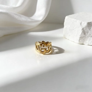 Anillo dorado minimalista con ondas caladas y detalles de puntos sobre seda