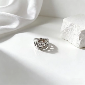 Detalle de anillo de acero inoxidable con ondas sobre satén blanco y piedra