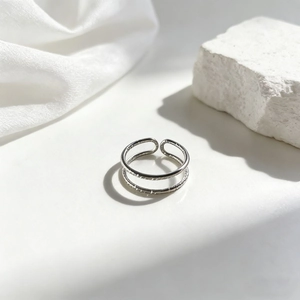 Detalle de anillo abierto de doble capa plateado con textura martillada y ajuste regulable