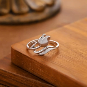 Primer plano de un anillo de tulipán plateado con hojas estilizadas en fondo madera