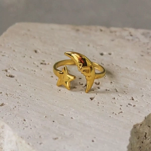 Detalle del anillo ajustable dorado con luna y estrella sobre fondo de piedra