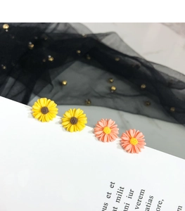 Detail of s925 daisy stud earrings in yellow and pink on a textured mesh background