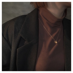 Detail van een gouden gematteerde kralenketting gedragen door een model met coltrui