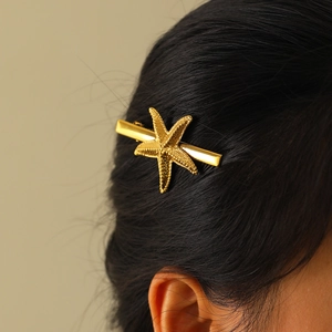Golden starfish hair clip with pearl texture detail on a dark hair background