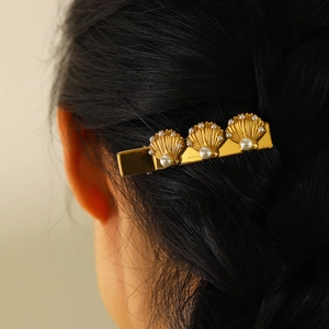 Detailed view of a golden shell hair clip with pearls on a dark braided hairstyle