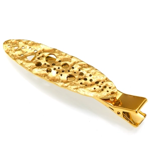 Detailed macro shot of golden textured metal hair clip with hollow oval cutout design
