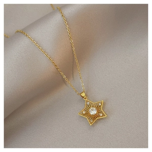 Close-up of a gold star pendant necklace with central zircon on grey silk fabric