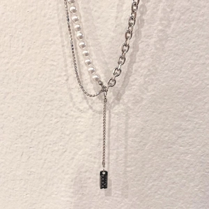 Hip hop layered necklace with ruler pendant, pearls, and rhinestones on white wall background