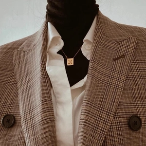 Collier doré avec pendentif carré lettre X porté sur un blazer à carreaux vintage