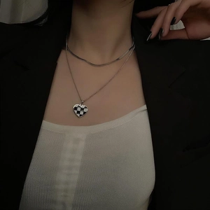 Detail showing a layered silver necklace with a heart-shaped checkerboard pendant on a model