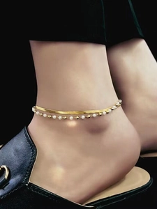 Detalle de tobillera de doble capa con cadena de espiga, perlas blancas y cuentas doradas