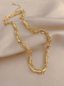 Détail d'un collier doré à maillons superposés sur fond en soie de couleur champagne