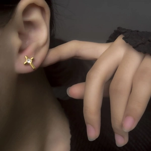 Close-up of a gold cross stud earring with a central zircon on a model's ear