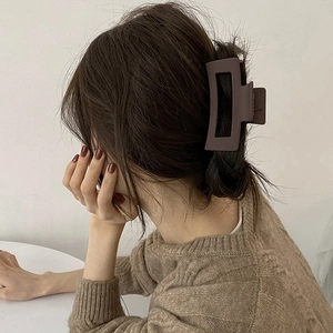 Detail of a matte dark brown rectangular hair claw clip on a model's wavy hair