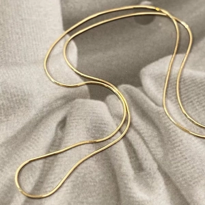 Détail d'un collier chaîne serpent doré sur un fond en tissu gris texturé élégant