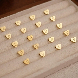 Golden heart-shaped initial pendant in stainless steel displayed on a beige velvet tray