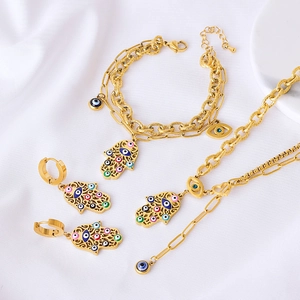 Detail of Hamsa and Evil Eye jewelry set featuring golden paperclip chains and enamel charms
