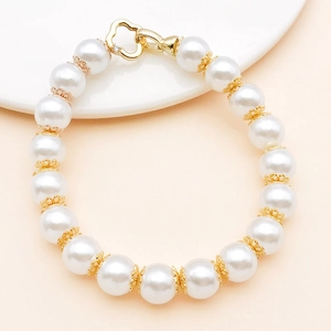Détail d'un bracelet en perles blanches avec intercalaires fleurs dorées et fermoir cœur