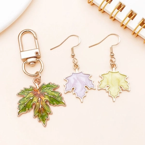 Detail of colorful enamel maple leaf keychain and matching earrings on a soft pink surface